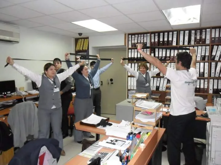 Grupo realizando ejercicios con bandas entre escritorios de oficina